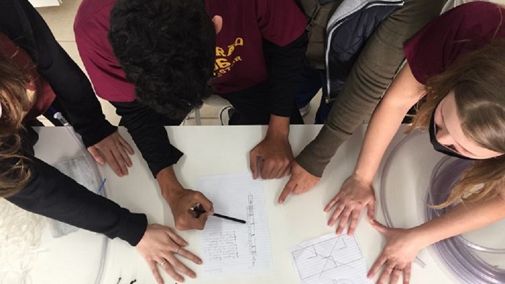 Três alunos e uma professora trabalhando em uma mesa branca