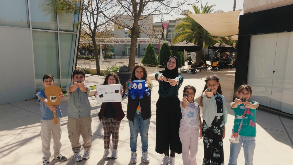 Rahaf em área externa junto a alunos de seu workshop, mostrando os projetos que criaram durante as aulas