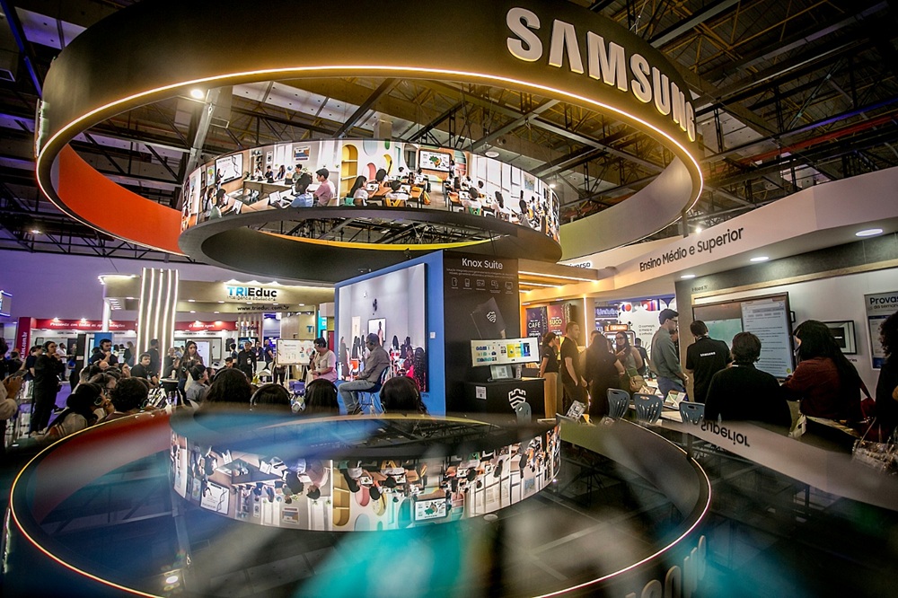 Imagem com reflexos mostra visitantes da Bett Brasil 2026 em palestra realizada no estande da Samsung durante o evento. 