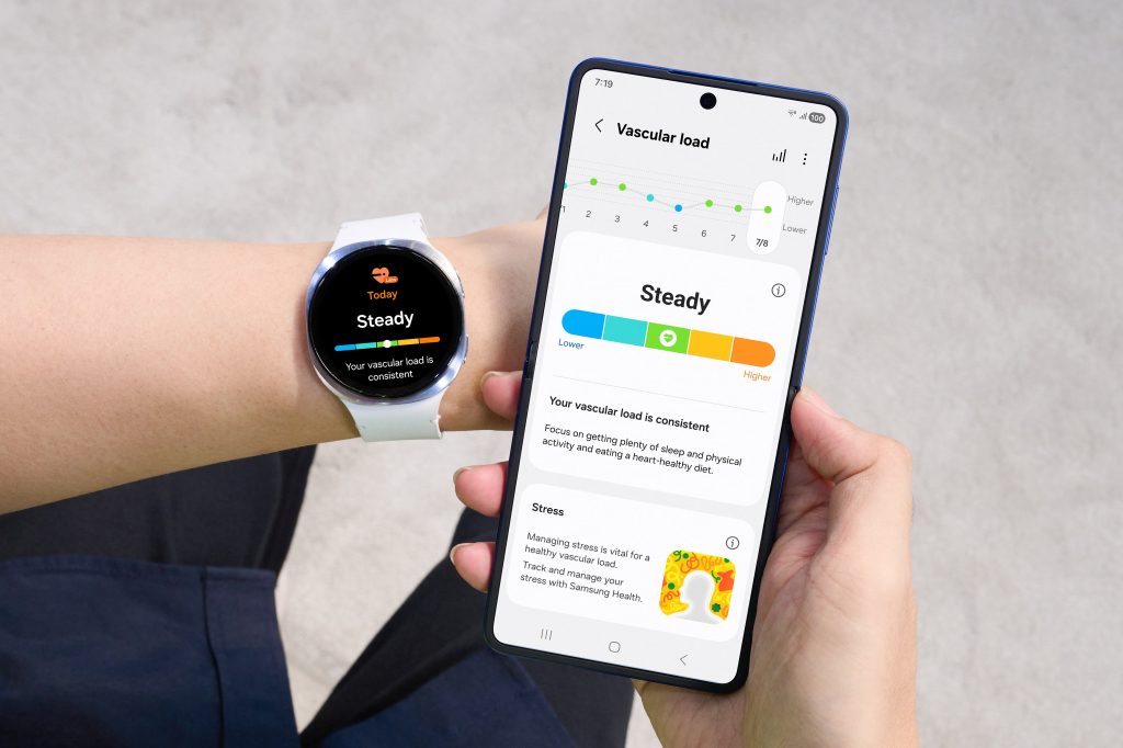 Pessoa segura um Galaxy Z Flip7 ao lado de um Galaxy Watch8 no pulso, com ambos mostrando informações sobre carga vascular e o status “Estável” para acompanhamento da saúde cardiovascular.