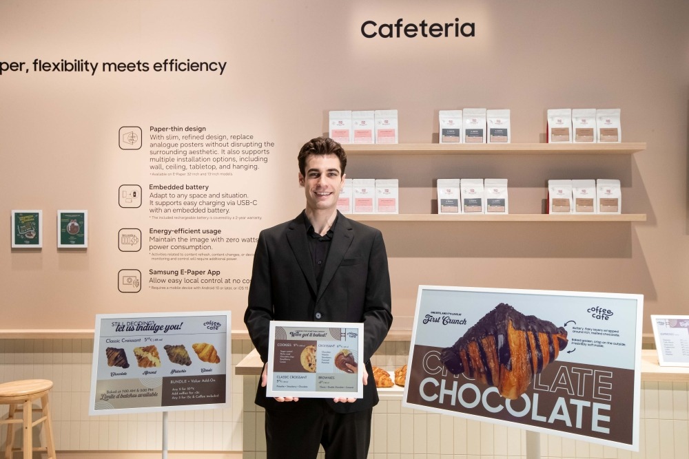 Um homem vestido de preto segura o Samsung Color E-Paper de 13 polegadas. Ele está cercado dos modelos de 20 e de 32 polegadas