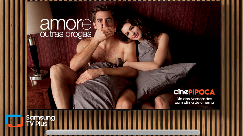 Imagem promocional do serviço Samsung TV Plus mostra uma TV Samsung, posicionada em um acabamento ripado de madeira, com cena do filme "Amor e outras drogas", disponível no canal Cine Pipoca, um dos canais do serviço gratuito, como parte da programação especial do serviço gratuito para o Dia dos Namorados.