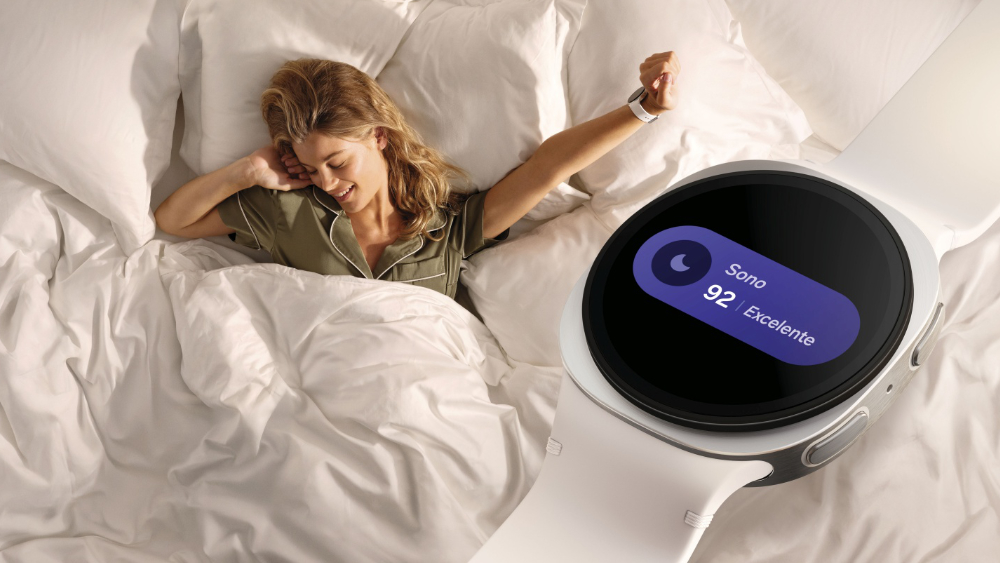 Vista superior de uma mulher sorrindo e se espreguiçando na cama, usando um Galaxy Watch8 no pulso. Em primeiro plano, uma ampliação da tela do relógio mostra o monitoramento do sono com pontuação 92 e classificação “Excelente”, destacando os recursos de acompanhamento do sono do dispositivo.