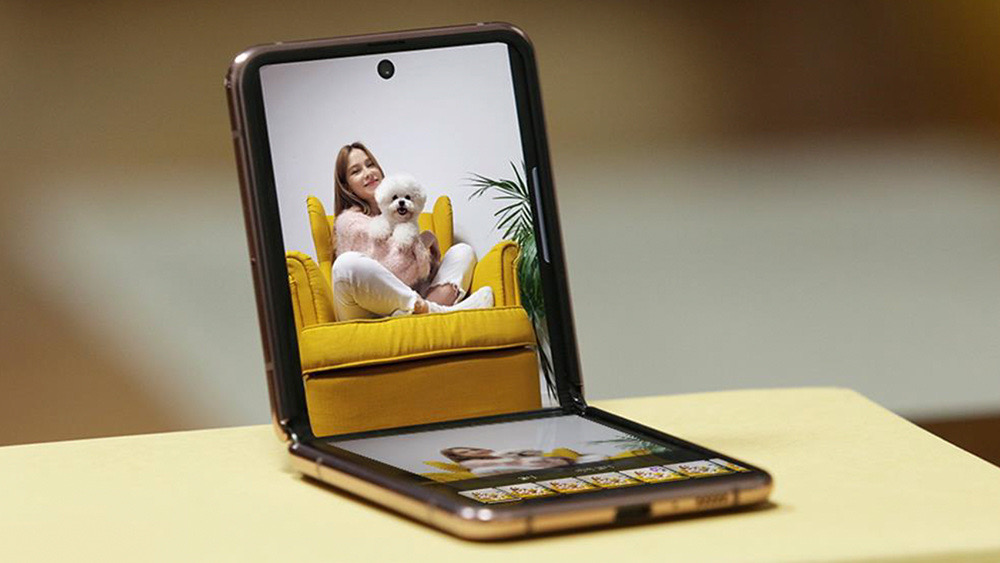 Imagem do Samsung Galaxy Z Flip2. A tela do aparelho está ligada e mostra uma menina segurando um cachorro em cima de uma poltrona amarela.