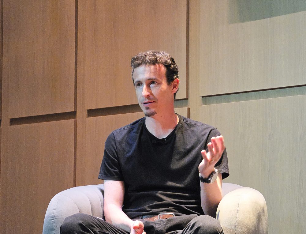 Otávio Penatti, chefe da equipe de P&D em AI para Saúde do Instituto de P&D da Samsung no Brasil, participa do painel sentado em uma poltrona, gesticulando enquanto apresenta sua visão sobre inteligência artificial aplicada à saúde.
