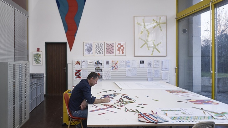 A imagem mostra o artista contemporâneo suíço Karim Noureldin em um retrato, vestindo uma camisa azul e posicionado em frente a um fundo claro.