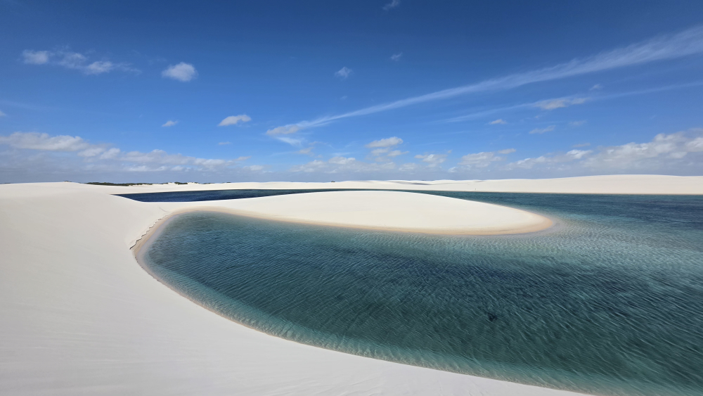 Lagoa de água cristalina entre dunas claras nos Lençóis Maranhenses sob céu azul.