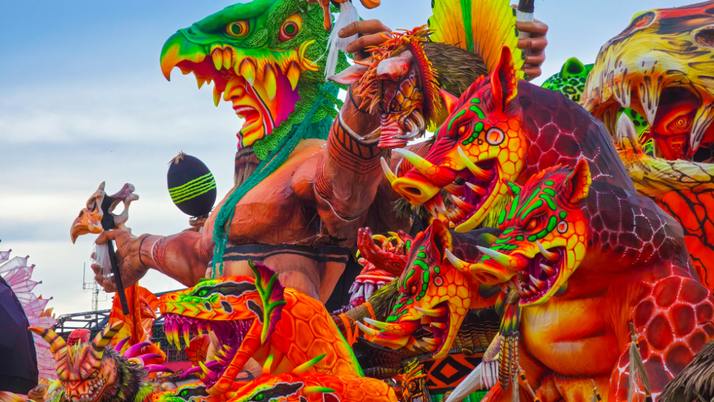 Carro alegórico do Festival de Parintins com esculturas coloridas de animais e personagens ocupando quase toda a imagem, sob céu nublado.
