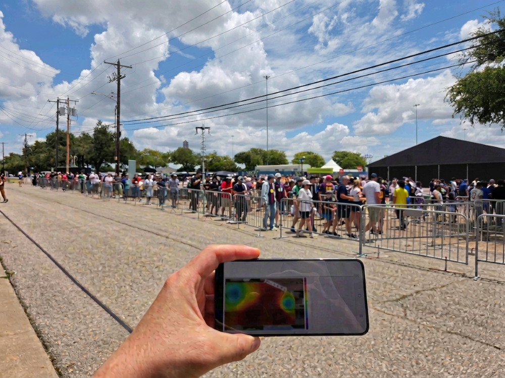 A imagem mostra um celular na mão de uma pessoa apontando na direção de uma multidão