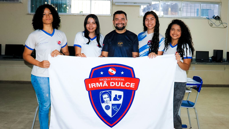 Professor e alunas de Parauapebas (PA) posam juntos com bandeira de instituição de ensino
