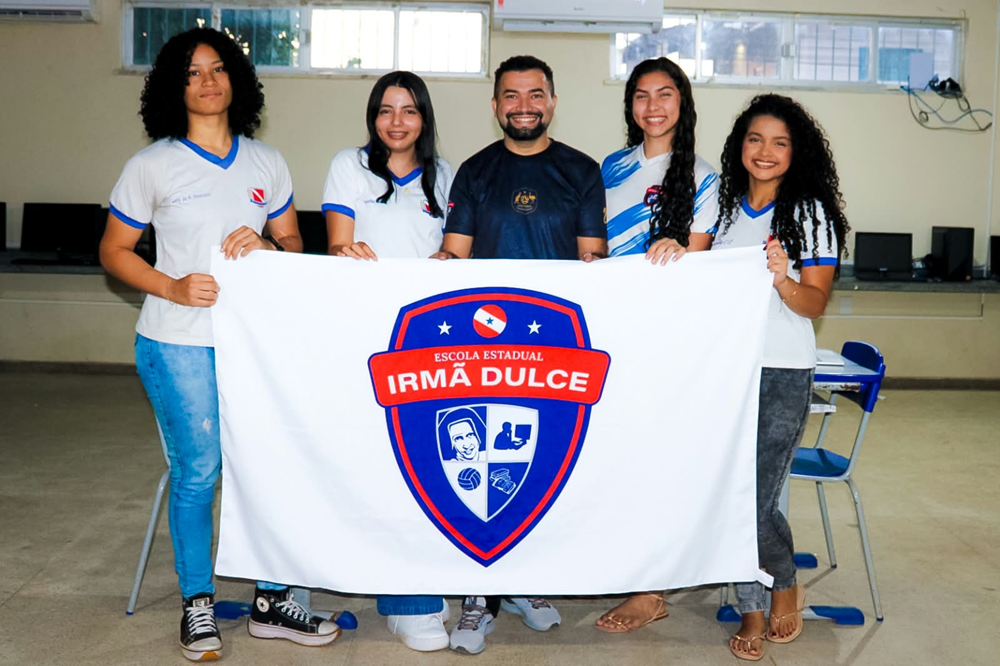 Professor e alunas de Parauapebas (PA) posam juntos com bandeira de instituição de ensino