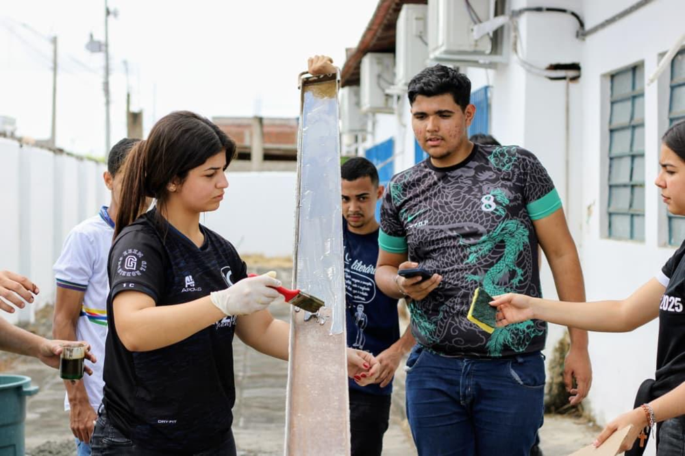 Estudantes participam de uma atividade prática ao lado de uma estrutura vertical, utilizando ferramentas e equipamentos para realizar testes e medições