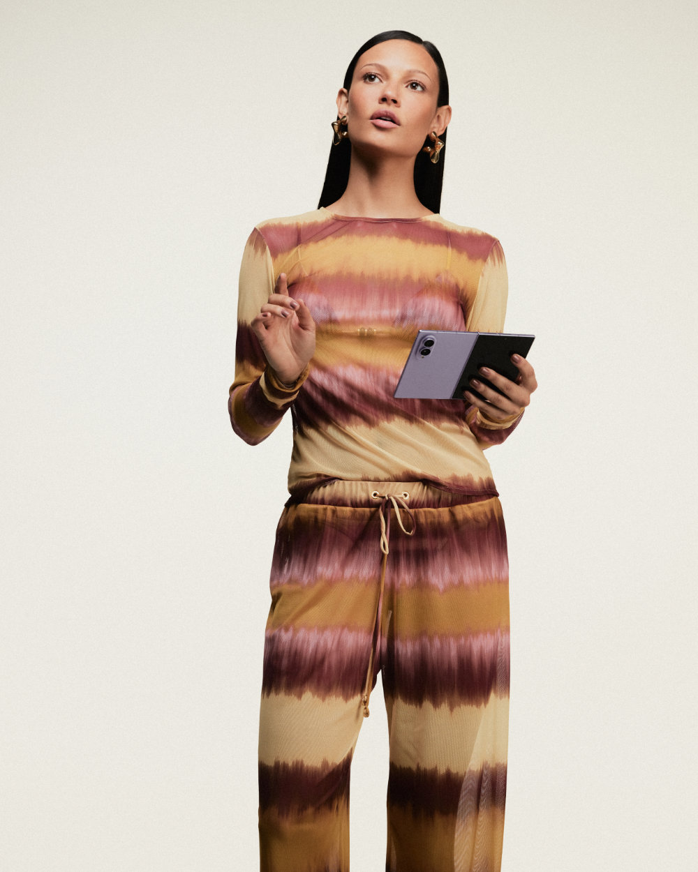 Modelo veste conjunto de blusa de manga longa e calça da coleção da ÁGUA DE COCO e segura um Galaxy Z Fold8 aberto nas mãos.