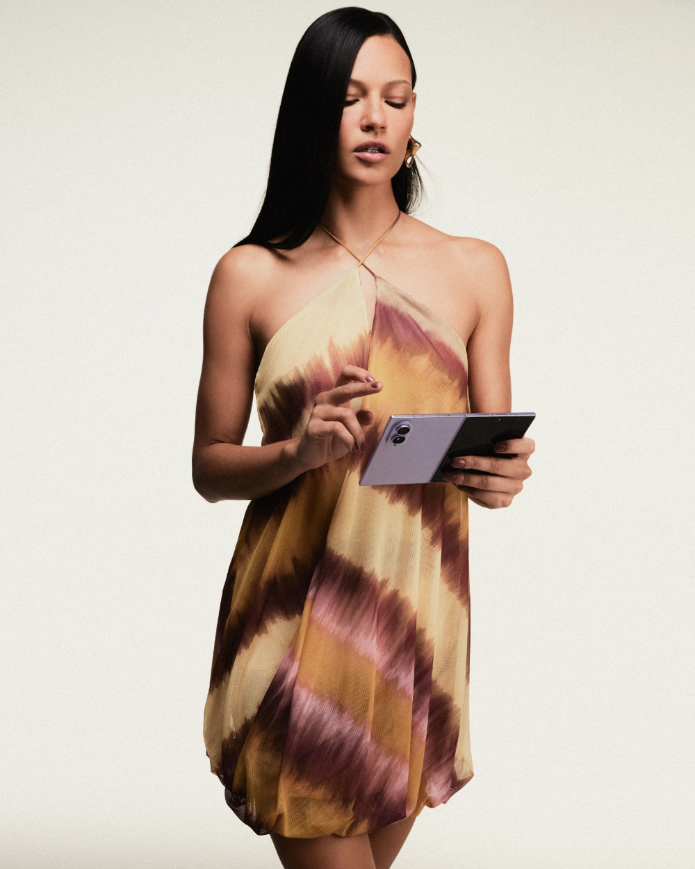 Modelo veste vestido estampado da coleção da ÁGUA DE COCO e segura um Galaxy Z Fold8 aberto enquanto toca na tela.