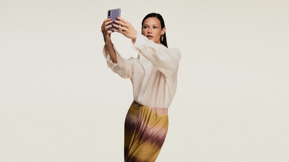 Modelo veste look da coleção ÁGUA DE COCO inspirada no Galaxy Z Fold8 e segura um Galaxy Z Fold8 na cor lavanda enquanto faz uma selfie.