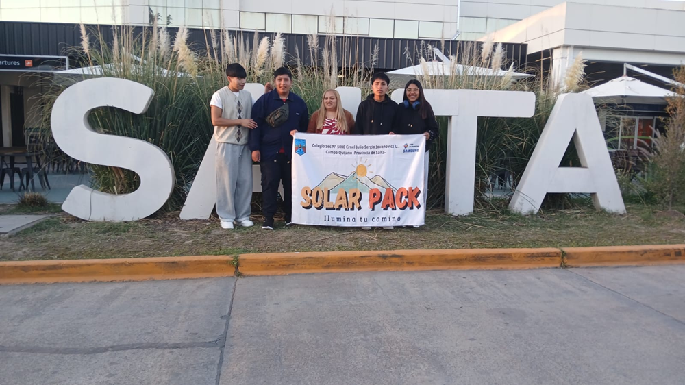 Professora argentina posa com seus alunos em frente à instituição de ensino segurando um banner do projeto Solar Pack.