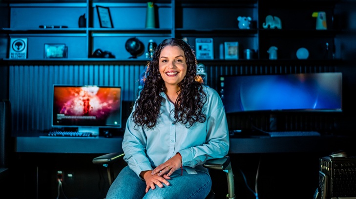 Marina Correia sentada em uma cadeira, em frente a um setup gamer, com produtos Samsung