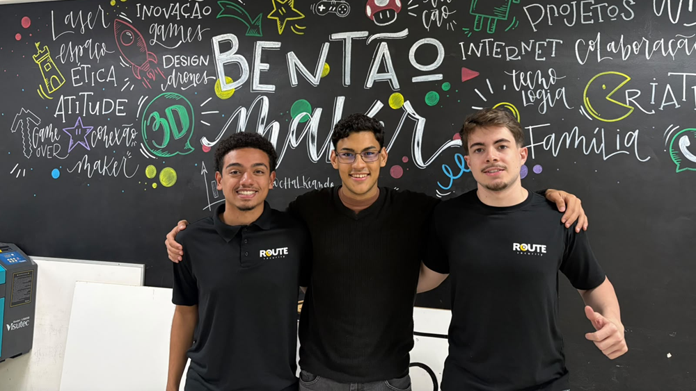 Três estudantes de escola técnica de Campinas, em São Paulo, posam juntos com um quadro preenchido com escritas ao fundo