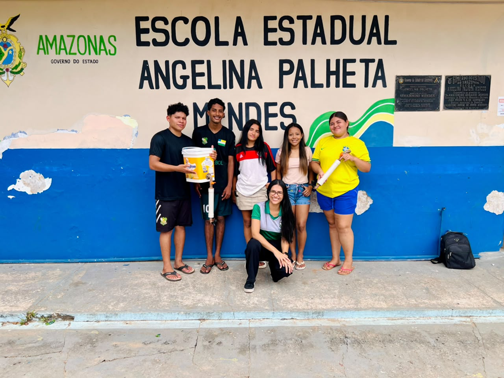 Grupo de dois alunos e três alunas posa junto a educadora em frente à escola estadual no Amazonas