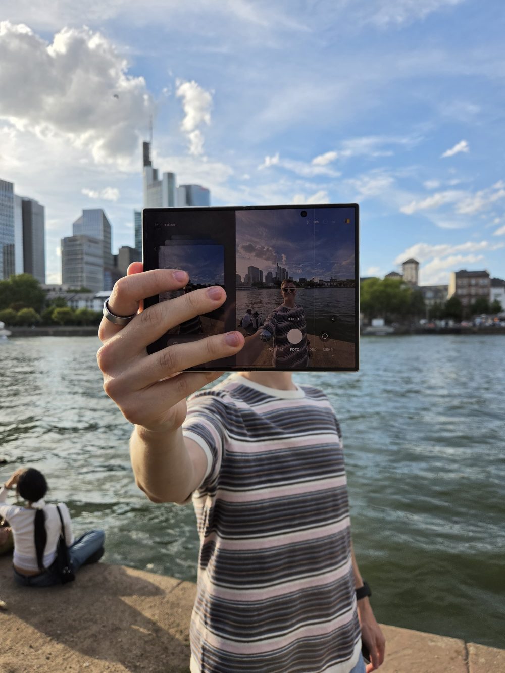 Eine Person hält ein aufgeklapptes Galaxy Z Fold8 vor die Frankfurter Skyline, um sich selbst zu fotografieren. Auf dem Display ist die Kameraansicht mit dem Motiv zu sehen. © Samsung Electronics