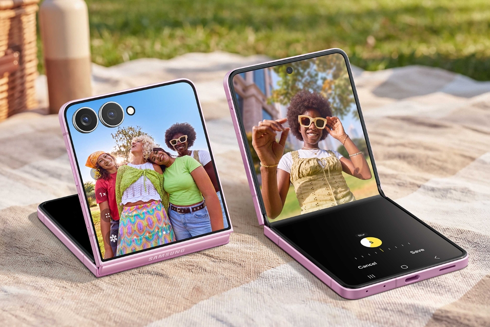 Zwei pinke Samsung Galaxy Z Flip8 liegen aufgeklappt im Flex-Modus auf einer Decke. Das linke Gerät zeigt ein Gruppenfoto, das rechte eine Nutzerin und eine Foto-Bearbeitungsansicht.