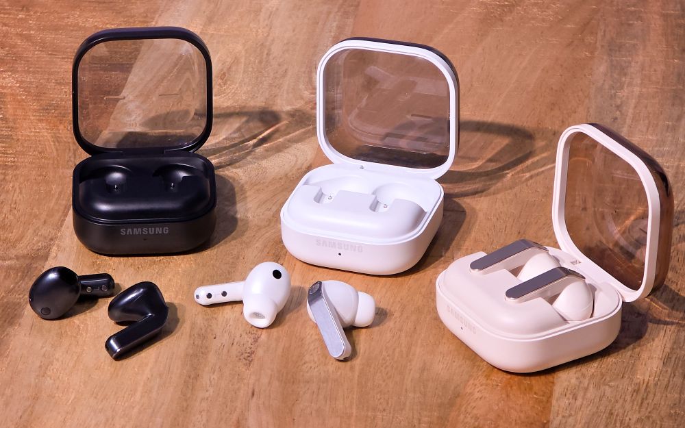 Drei geöffnete Ladecases der Samsung Galaxy Buds4 und Samsung Galaxy Buds4 Pro liegen auf einer Holzfläche.
