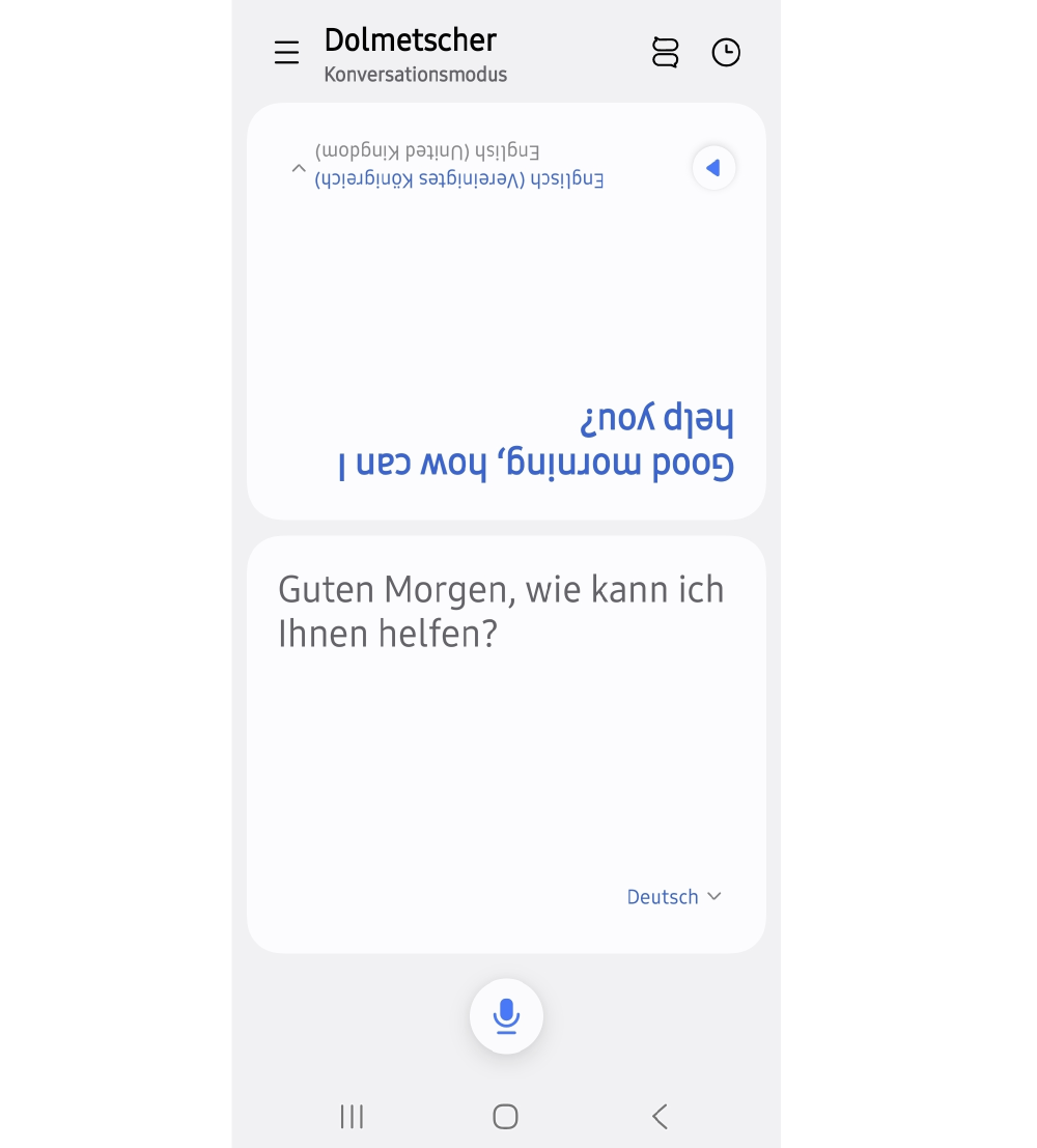 Screenshot der Dolmetscher-App eines Samsung Galaxy Smartphones im Konversationsmodus: Der Satz „Guten Morgen, wie kann ich Ihnen helfen?“ erscheint auf Deutsch in der unteren Bildschirmhälfte und um 180 Grad gedreht als englische Übersetzung „Good morning, how can I help you?“ in der oberen Hälfte.