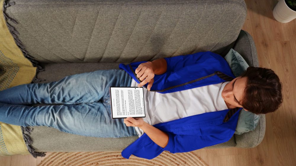 Vogelperspektive auf eine Person, die auf einem grauen Sofa liegt und ein aufgeklapptes Samsung Galaxy Z Fold8 in beiden Händen hält. Auf dem Hauptdisplay ist ein Text zu lesen. © Samsung Electronics