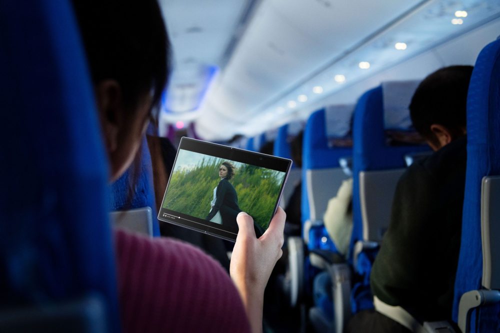 Eine Person sitzt in einem Flugzeug und hält ein aufgeklapptes Samsung Galaxy Z Fold8 in der Hand. Auf dem Hauptdisplay ist eine Filmszene zu sehen. Im Hintergrund sind die blauen Sitze der Flugzeugkabine und weitere Passagiere zu erkennen. © Samsung Electronics