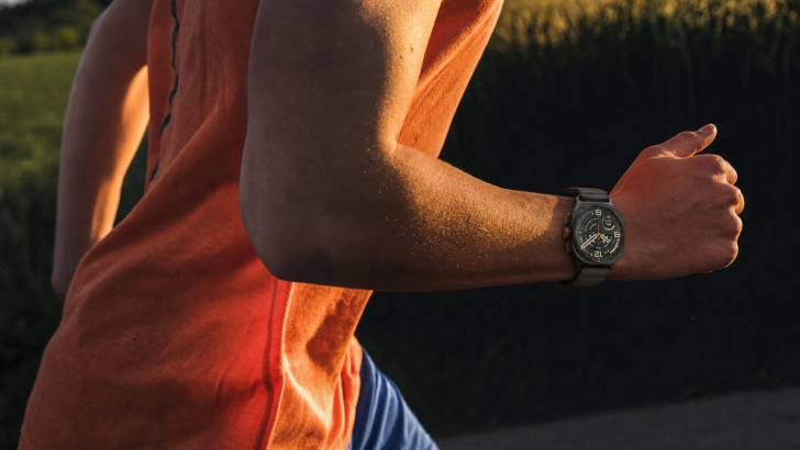 Nahaufnahme eines Läufers im orangefarbenen Shirt. Am Handgelenk trägt er die Samsung Galaxy Watch Ultra2 in Titanium Gray. Im Hintergrund grünes Gebüsch im Gegenlicht der Abendsonne. © Samsung Electronics