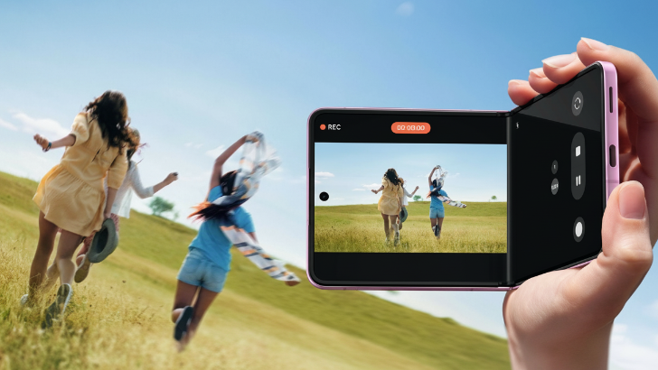 Eine Frauenhand hält ein rechtwinklig aufgeklapptes Samsung Galaxy Z Flip8. Auf dem Display und im Hintergrund sieht man drei Frauen, die über eine Wiese laufen.