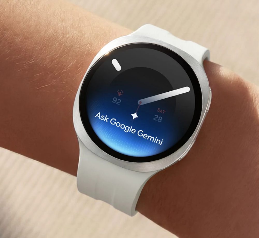 Silberfarbene Samsung Galaxy Watch9 mit weißem Armband an einem Handgelenk; auf dem schwarzen Display steht „Ask Google Gemini“.