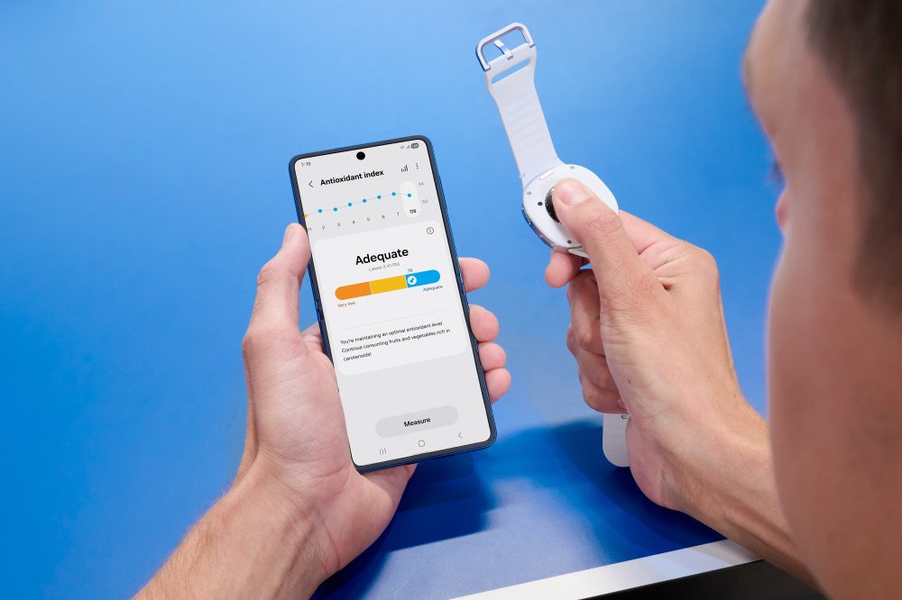 Messung des Antioxidantien-Index mit einer Samsung Galaxy Watch: Eine Person drückt den rechten Daumen auf den rückseitigen Sensor der abgenommenen Smartwatch, während auf dem Samsung Galaxy Smartphone in der linken Hand das Ergebnis „Adequate“ (Wert 78) in der Samsung Health-App angezeigt wird.