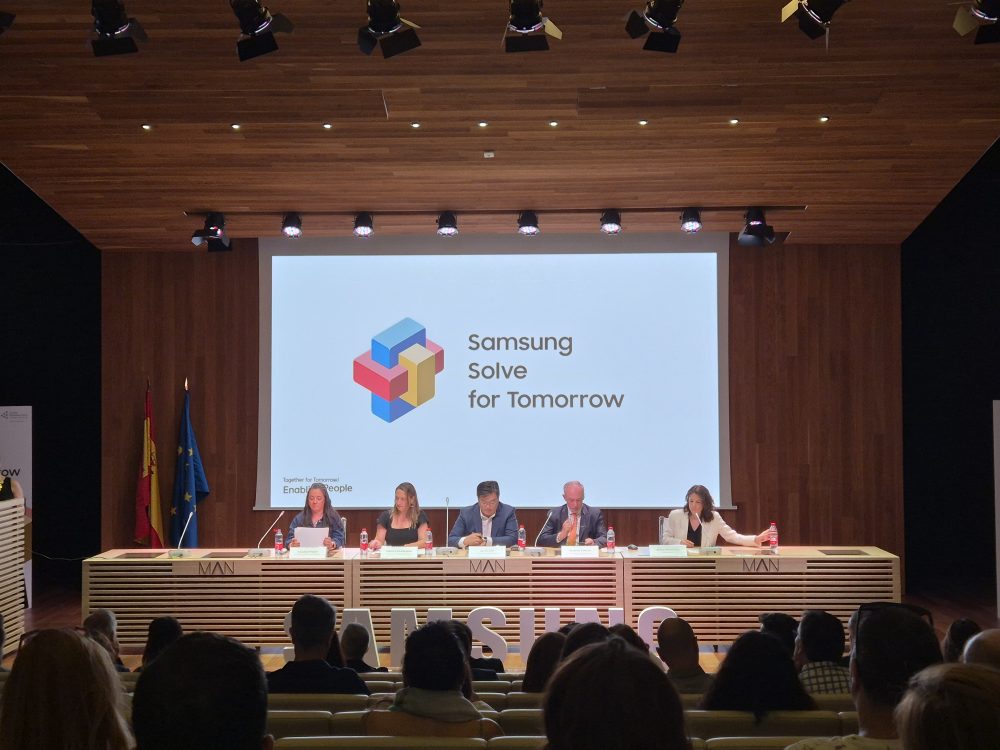 Ponentes en el escenario durante un evento de Samsung Solve for Tomorrow, con el logotipo del programa proyectado en una gran pantalla frente a una audiencia.