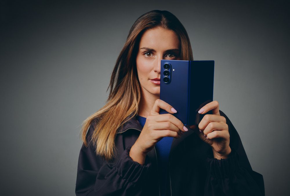 Alexia Putellas muestra un smartphone plegable Samsung Galaxy azul en una imagen promocional que resalta el diseño plegable y la experiencia Galaxy.