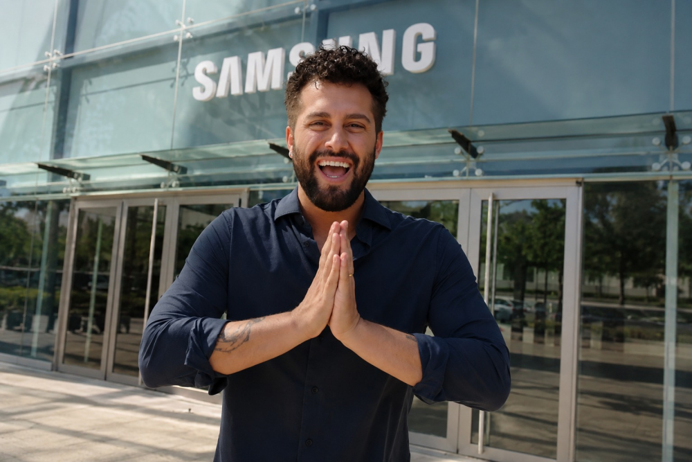 Javi Hoyos sonríe con las manos juntas frente a la entrada de un edificio de Samsung.