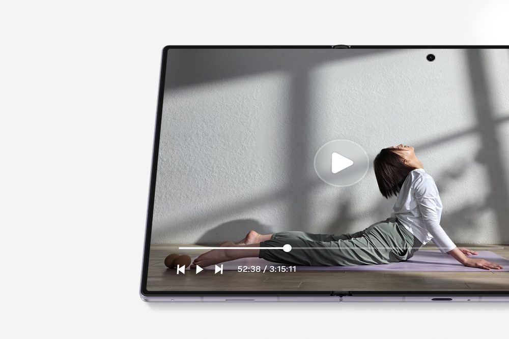 Samsung Galaxy Z Fold8 shown unfolded with a video playing across its large main display, featuring a person exercising and on-screen playback controls.