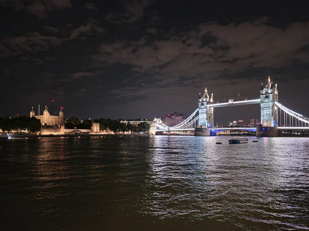 Tower Bridge and the Tower of London illuminated at night beside the River Thames, with city lights reflected on the water.