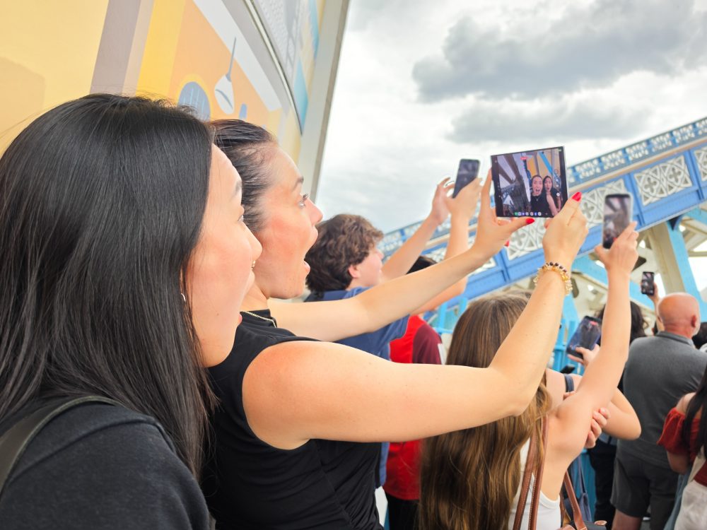 Visitors take photos near Tower Bridge in London, while a woman uses an unfolded Samsung Galaxy foldable smartphone to capture a selfie.