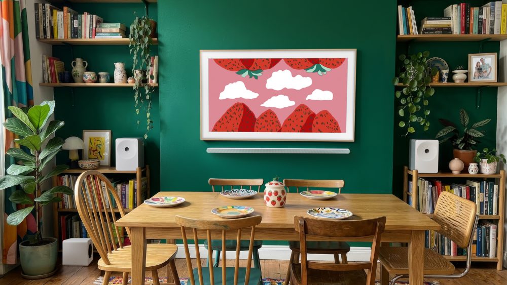 The Frame integrado en un comedor con pared verde, mostrando una ilustración en pantalla y formando parte de la decoración junto a estanterías, libros y plantas.