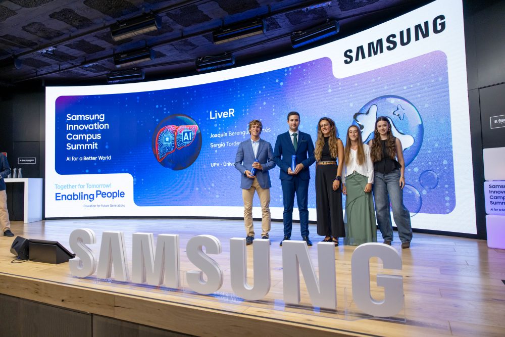 Cinco participantes posan en el escenario del Samsung Innovation Campus Summit, frente a una gran pantalla del evento y junto a las letras de Samsung.