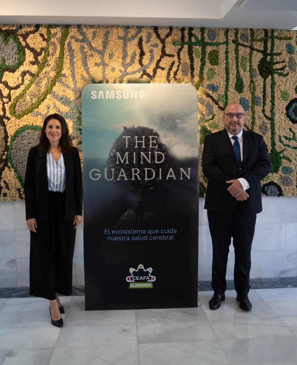 Dos personas posan junto al panel de Samsung de The Mind Guardian: El ecosistema que cuida nuestra salud cerebral, con el logotipo de CEAFA Alzheimer.