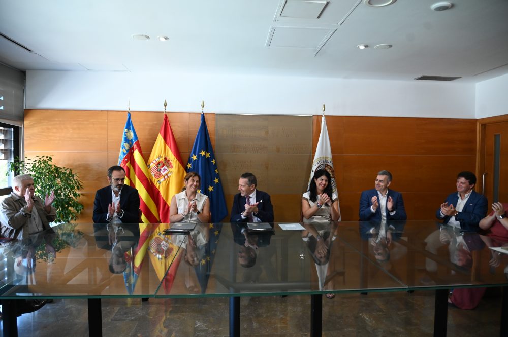 Representantes aplauden tras la firma de un acuerdo en la Universitat Politècnica de València, con las banderas de la Comunidad Valenciana, España, la Unión Europea y la UPV al fondo.