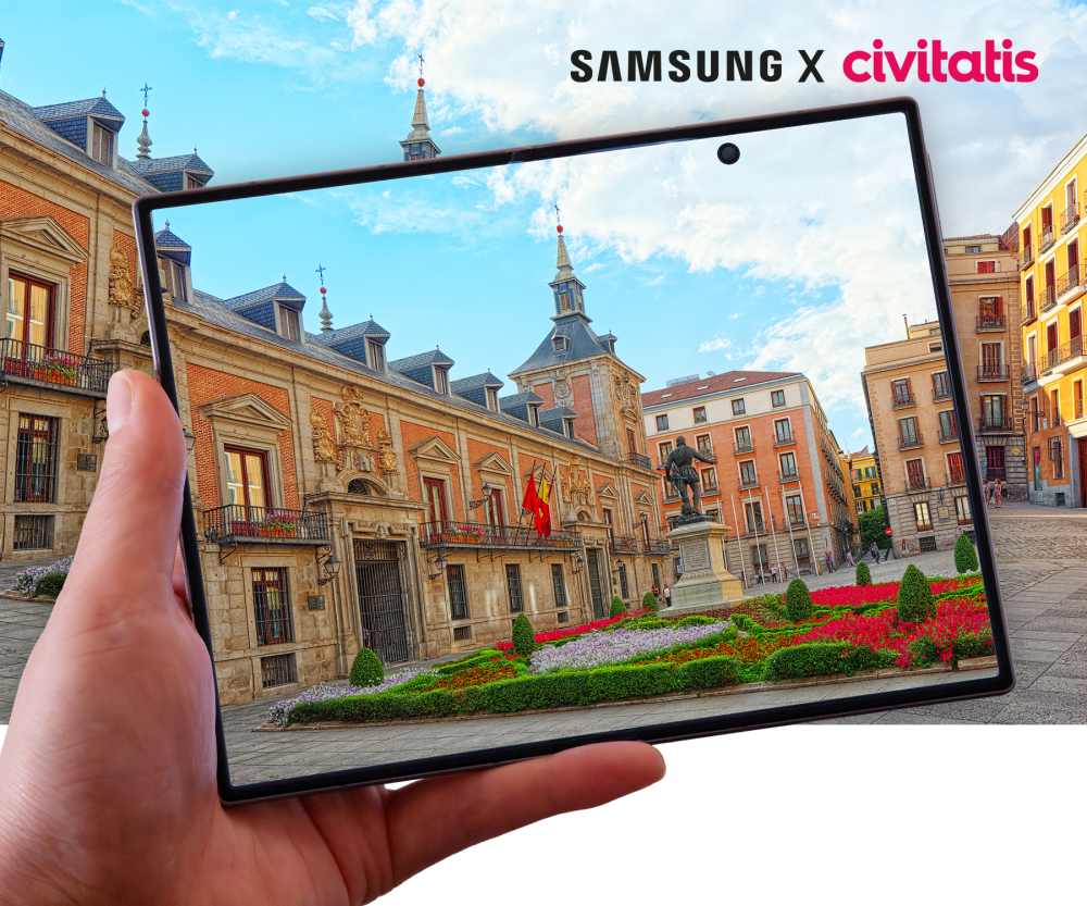Imagen de la colaboración Samsung x Civitatis en la que una mano sostiene una tablet Samsung Galaxy frente a la Plaza de la Villa de Madrid, mostrando en pantalla el edificio histórico y sus jardines.