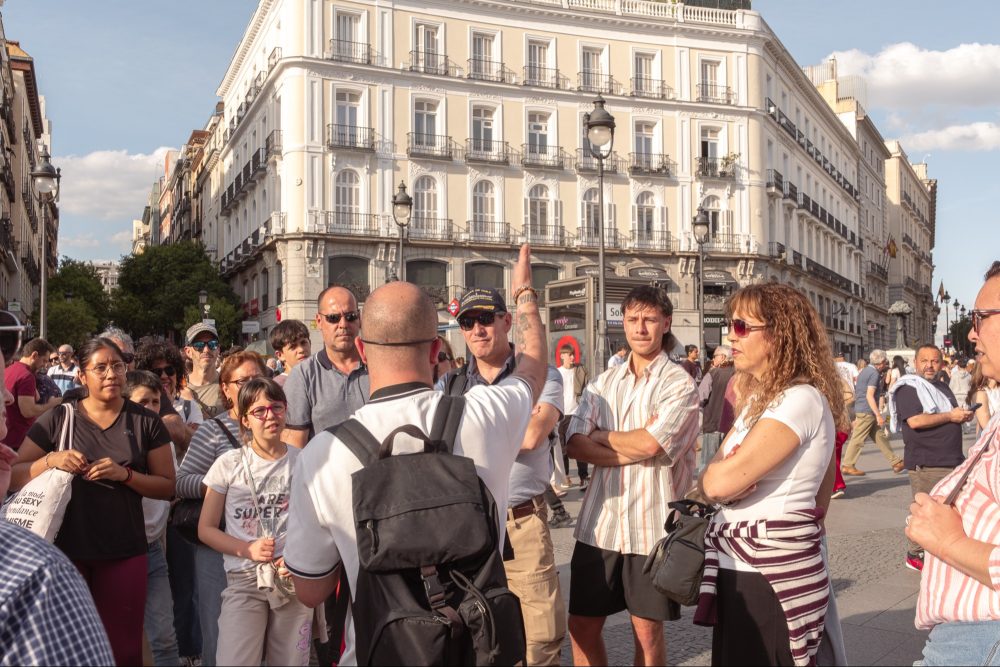 Un guía turístico explica la historia de la Puerta del Sol de Madrid a un grupo de visitantes durante una visita guiada, frente a los edificios históricos de la plaza.