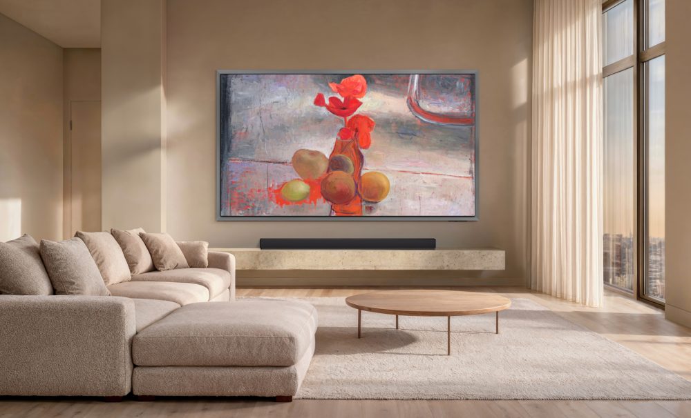 Samsung OLED S95H instalada en la pared de un salón moderno y luminoso, mostrando una obra de arte floral de Art Store, con sofá beige y barra de sonido.