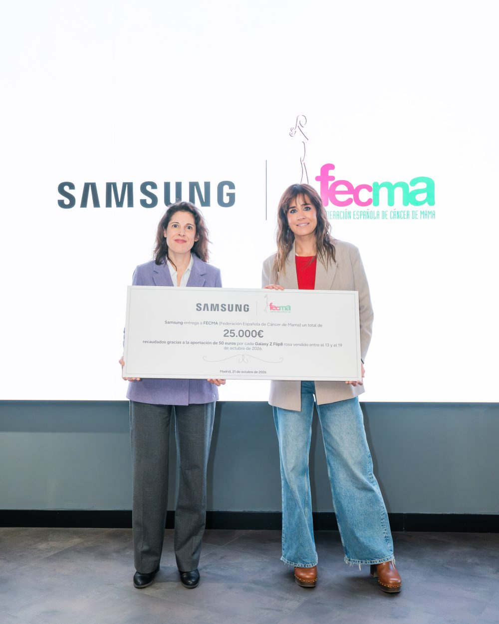 Dos representantes posan con un cheque solidario de 25.000 euros de Samsung a FECMA (Federación Española de Cáncer de Mama), recaudados mediante la aportación de 50 euros por cada Galaxy Z Flip8 rosa vendido durante la campaña contra el cáncer de mama.