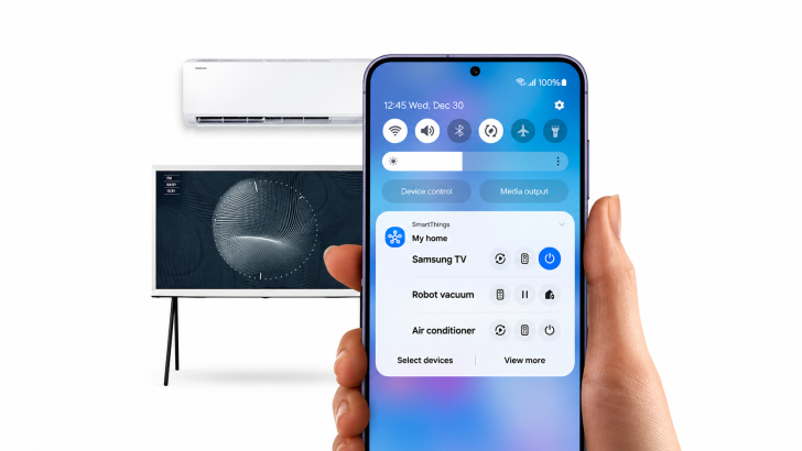 Un smartphone Samsung Galaxy muestra la aplicación SmartThings con controles para gestionar un televisor Samsung, un robot aspirador y un aire acondicionado en un hogar conectado.