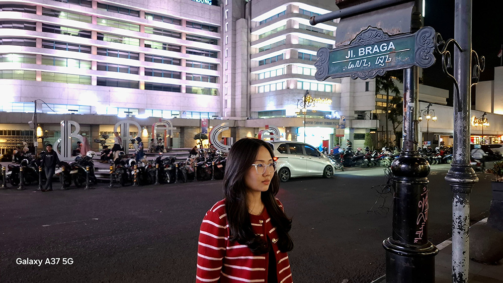 Seorang perempuan direkam di depan rambu jalan malam hari dengan fitur Nightography Video Galaxy A37 5G.