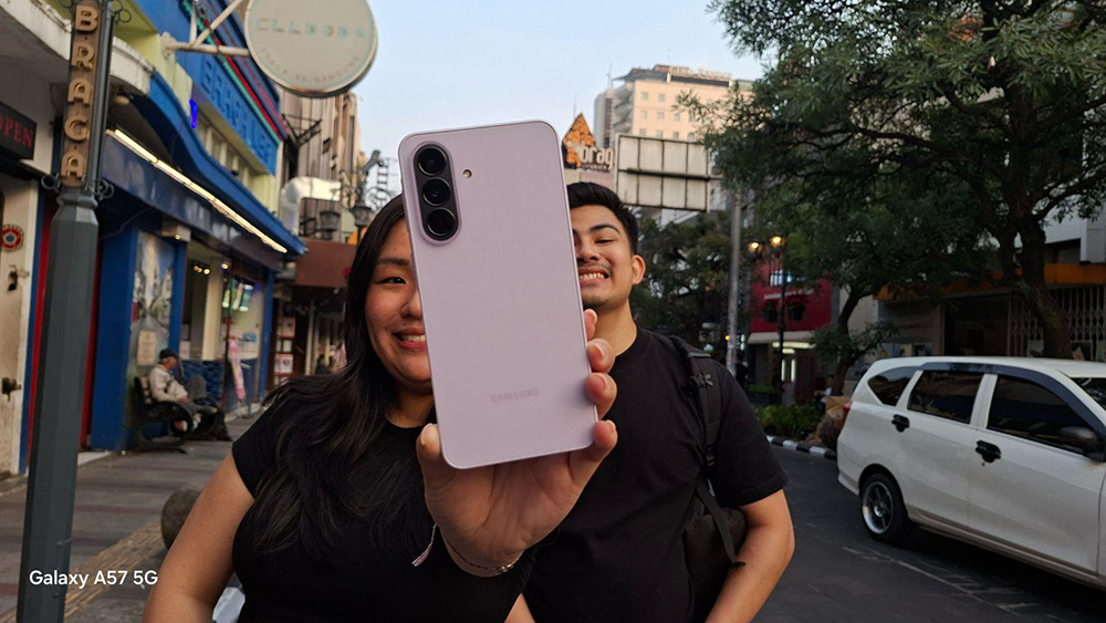 Perempuan memegang Samsung Galaxy A57 5G di jalanan kota, amengabadikan momen dengan fitur Camera Assistant dari Good Lock.